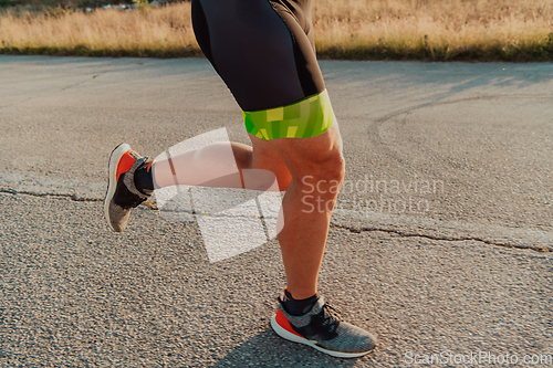 Image of Closeup of muscular legs of a triathlete in professional equipment running early in the morning, preparing for a marathon, dedication to sports and readiness for marathon challenges