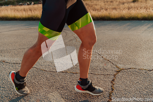 Image of Closeup of muscular legs of a triathlete in professional equipment running early in the morning, preparing for a marathon, dedication to sports and readiness for marathon challenges