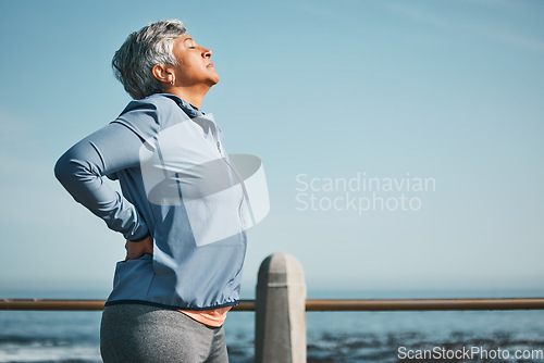 Image of Tired, running and senior woman pain from back ache by the ocean for fitness, exercise and workout. Runner, person with sport outdoor on beach with muscle strain and athlete injury on mockup space