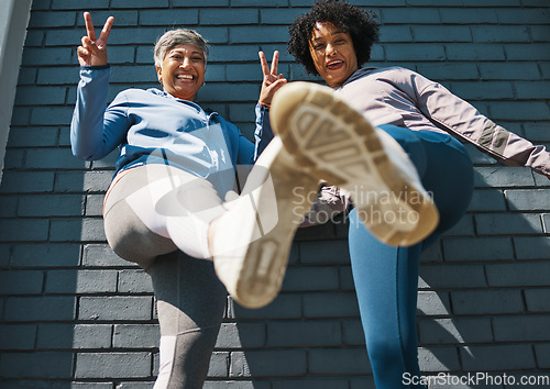 Image of Bottom view, shoes and women with portrait, peace sign and smile outdoor. Wall, mature female friends and urban fitness feet with exercise sneakers, fashion and happy, v and emoji hand gesture