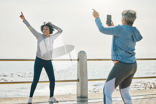 Image of Photograph, senior woman and friends fitness with social media post feeling silly by the sea. Training, exercise and workout with mature people and photo for profile picture with pointing by ocean