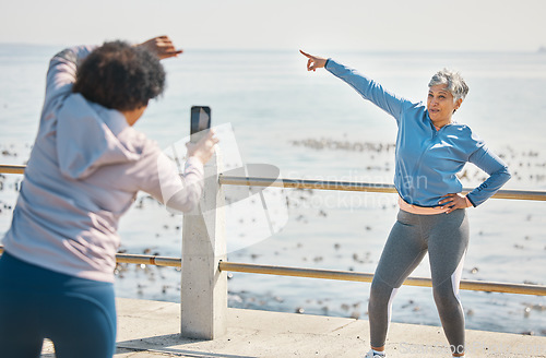 Image of Phone, friends and photo of senior woman pointing at beach with silly pose at sea for fitness. Exercise, mobile and picture for social media post on a ocean promenade walk for workout and friendship