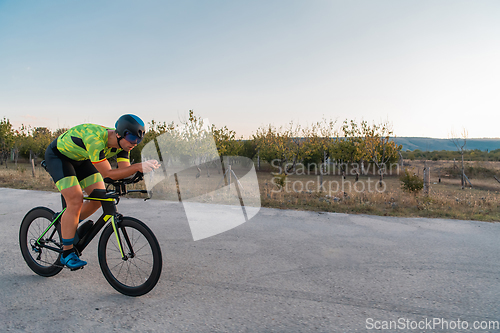 Image of Triathlete riding his bicycle during sunset, preparing for a marathon. The warm colors of the sky provide a beautiful backdrop for his determined and focused effort.