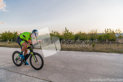 Image of Triathlete riding his bicycle during sunset, preparing for a marathon. The warm colors of the sky provide a beautiful backdrop for his determined and focused effort.