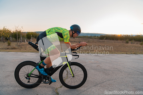 Image of Triathlete riding his bicycle during sunset, preparing for a marathon. The warm colors of the sky provide a beautiful backdrop for his determined and focused effort.