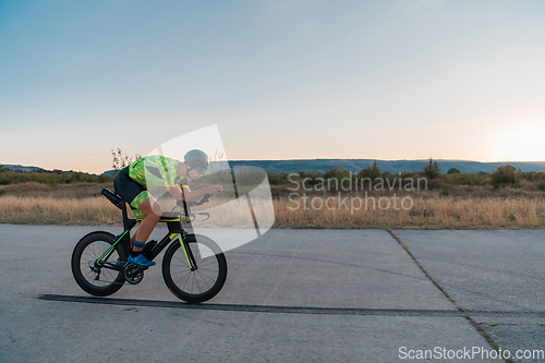 Image of Triathlete riding his bicycle during sunset, preparing for a marathon. The warm colors of the sky provide a beautiful backdrop for his determined and focused effort.