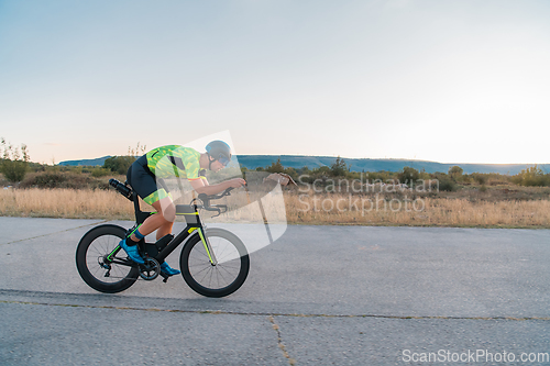 Image of Triathlete riding his bicycle during sunset, preparing for a marathon. The warm colors of the sky provide a beautiful backdrop for his determined and focused effort.