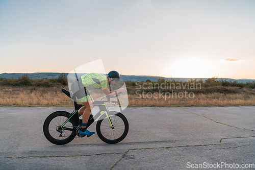 Image of Triathlete riding his bicycle during sunset, preparing for a marathon. The warm colors of the sky provide a beautiful backdrop for his determined and focused effort.