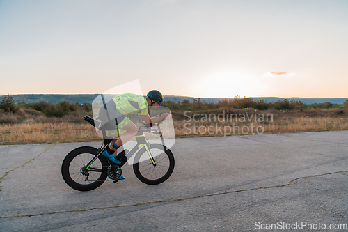 Image of Triathlete riding his bicycle during sunset, preparing for a marathon. The warm colors of the sky provide a beautiful backdrop for his determined and focused effort.