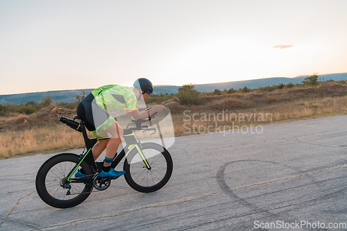 Image of Triathlete riding his bicycle during sunset, preparing for a marathon. The warm colors of the sky provide a beautiful backdrop for his determined and focused effort.