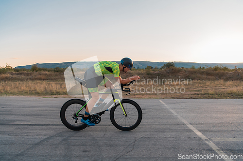 Image of Triathlete riding his bicycle during sunset, preparing for a marathon. The warm colors of the sky provide a beautiful backdrop for his determined and focused effort.