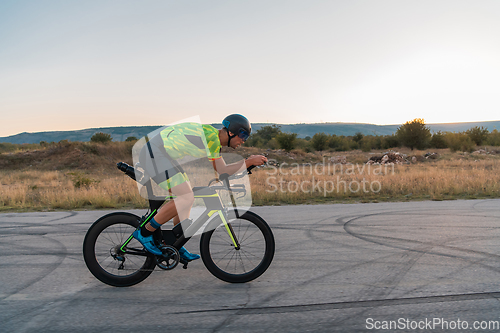 Image of Triathlete riding his bicycle during sunset, preparing for a marathon. The warm colors of the sky provide a beautiful backdrop for his determined and focused effort.