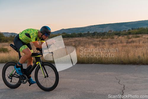 Image of Triathlete riding his bicycle during sunset, preparing for a marathon. The warm colors of the sky provide a beautiful backdrop for his determined and focused effort.