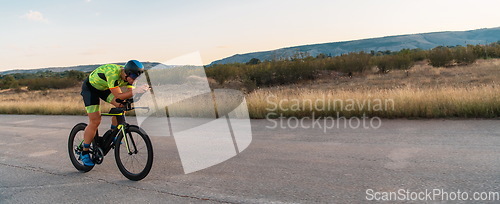 Image of Triathlete riding his bicycle during sunset, preparing for a marathon. The warm colors of the sky provide a beautiful backdrop for his determined and focused effort.