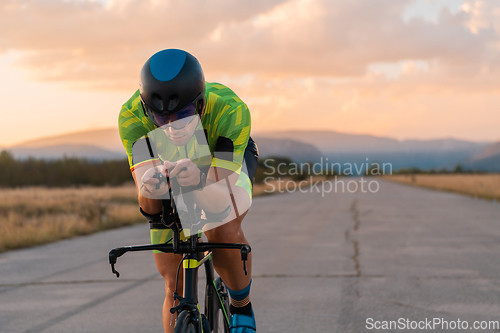 Image of Triathlete riding his bicycle during sunset, preparing for a marathon. The warm colors of the sky provide a beautiful backdrop for his determined and focused effort.