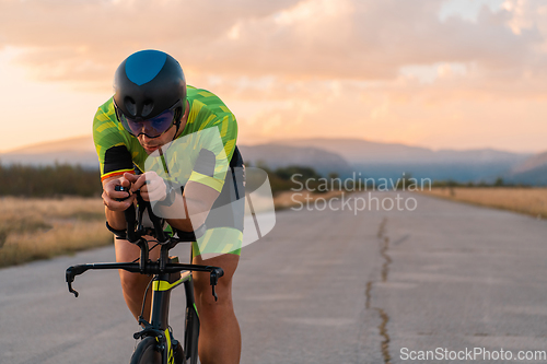 Image of Triathlete riding his bicycle during sunset, preparing for a marathon. The warm colors of the sky provide a beautiful backdrop for his determined and focused effort.