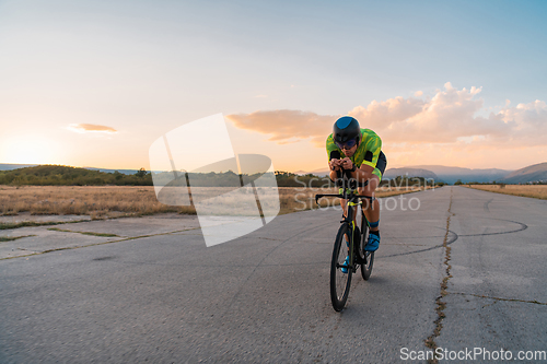 Image of Triathlete riding his bicycle during sunset, preparing for a marathon. The warm colors of the sky provide a beautiful backdrop for his determined and focused effort.