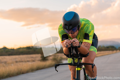 Image of Triathlete riding his bicycle during sunset, preparing for a marathon. The warm colors of the sky provide a beautiful backdrop for his determined and focused effort.