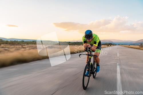 Image of Triathlete riding his bicycle during sunset, preparing for a marathon. The warm colors of the sky provide a beautiful backdrop for his determined and focused effort.