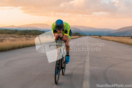 Image of Triathlete riding his bicycle during sunset, preparing for a marathon. The warm colors of the sky provide a beautiful backdrop for his determined and focused effort.