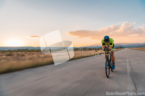 Image of Triathlete riding his bicycle during sunset, preparing for a marathon. The warm colors of the sky provide a beautiful backdrop for his determined and focused effort.