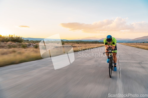 Image of Triathlete riding his bicycle during sunset, preparing for a marathon. The warm colors of the sky provide a beautiful backdrop for his determined and focused effort.