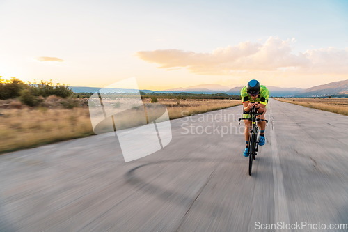 Image of Triathlete riding his bicycle during sunset, preparing for a marathon. The warm colors of the sky provide a beautiful backdrop for his determined and focused effort.