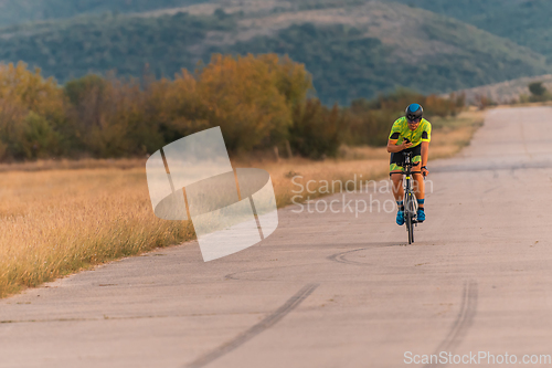 Image of Triathlete riding his bicycle during sunset, preparing for a marathon. The warm colors of the sky provide a beautiful backdrop for his determined and focused effort.