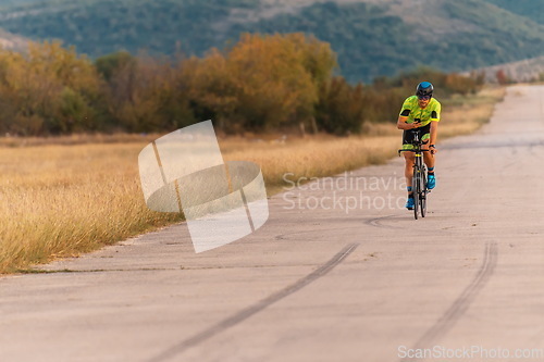 Image of Triathlete riding his bicycle during sunset, preparing for a marathon. The warm colors of the sky provide a beautiful backdrop for his determined and focused effort.