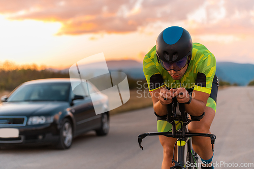 Image of Close up photo of triathlete riding his bicycle during sunset, preparing for a marathon. The warm colors of the sky provide a beautiful backdrop for his determined and focused effort.