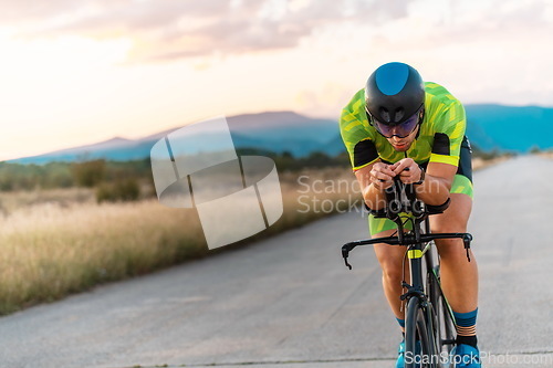 Image of Triathlete riding his bicycle during sunset, preparing for a marathon. The warm colors of the sky provide a beautiful backdrop for his determined and focused effort.