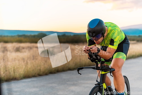 Image of Triathlete riding his bicycle during sunset, preparing for a marathon. The warm colors of the sky provide a beautiful backdrop for his determined and focused effort.