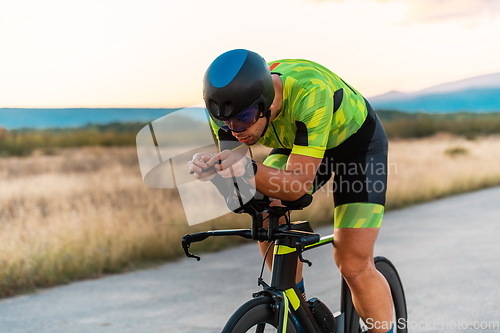 Image of Triathlete riding his bicycle during sunset, preparing for a marathon. The warm colors of the sky provide a beautiful backdrop for his determined and focused effort.