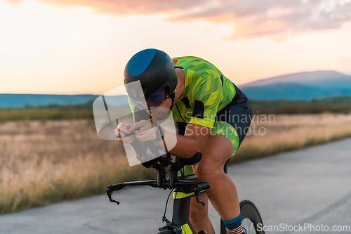 Image of Close up photo of triathlete riding his bicycle during sunset, preparing for a marathon. The warm colors of the sky provide a beautiful backdrop for his determined and focused effort.