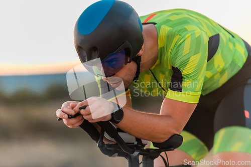 Image of Close up photo of triathlete riding his bicycle during sunset, preparing for a marathon. The warm colors of the sky provide a beautiful backdrop for his determined and focused effort.