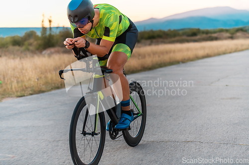 Image of Triathlete riding his bicycle during sunset, preparing for a marathon. The warm colors of the sky provide a beautiful backdrop for his determined and focused effort.