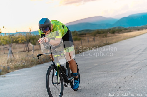 Image of Triathlete riding his bicycle during sunset, preparing for a marathon. The warm colors of the sky provide a beautiful backdrop for his determined and focused effort.