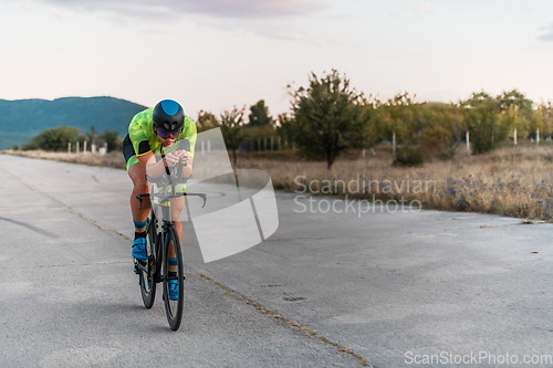 Image of Triathlete riding his bicycle during sunset, preparing for a marathon. The warm colors of the sky provide a beautiful backdrop for his determined and focused effort.