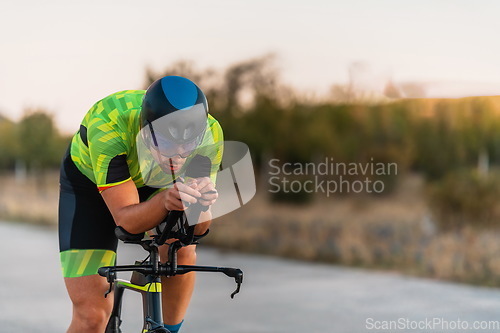 Image of Triathlete riding his bicycle during sunset, preparing for a marathon. The warm colors of the sky provide a beautiful backdrop for his determined and focused effort.