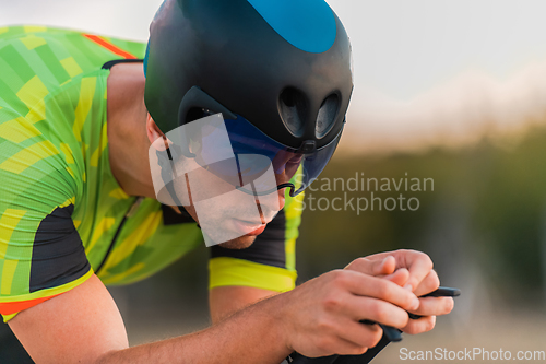 Image of Close up photo of triathlete riding his bicycle during sunset, preparing for a marathon. The warm colors of the sky provide a beautiful backdrop for his determined and focused effort.