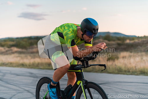 Image of Triathlete riding his bicycle during sunset, preparing for a marathon. The warm colors of the sky provide a beautiful backdrop for his determined and focused effort.