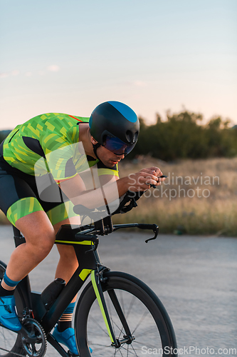 Image of Triathlete riding his bicycle during sunset, preparing for a marathon. The warm colors of the sky provide a beautiful backdrop for his determined and focused effort.