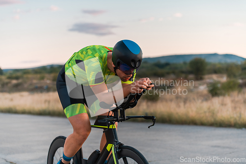 Image of Triathlete riding his bicycle during sunset, preparing for a marathon. The warm colors of the sky provide a beautiful backdrop for his determined and focused effort.