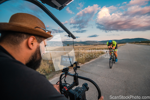 Image of A videographer recording a triathlete riding his bike preparing for an upcoming marathon.Athlete's physical endurance and the dedication required to succeed in the sport.