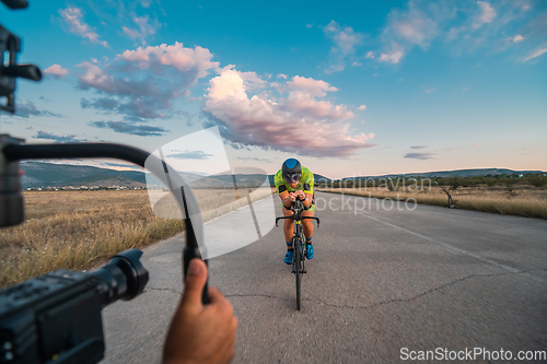 Image of A videographer recording a triathlete riding his bike preparing for an upcoming marathon.Athlete's physical endurance and the dedication required to succeed in the sport.