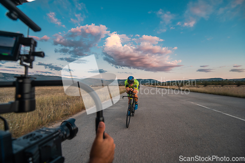 Image of A videographer recording a triathlete riding his bike preparing for an upcoming marathon.Athlete's physical endurance and the dedication required to succeed in the sport.