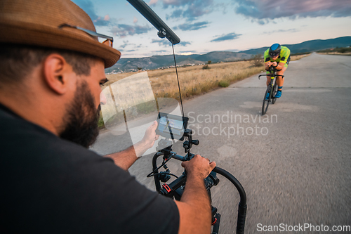 Image of A videographer recording a triathlete riding his bike preparing for an upcoming marathon.Athlete's physical endurance and the dedication required to succeed in the sport.