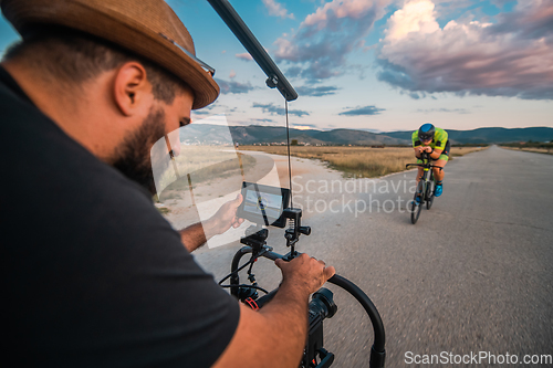 Image of A videographer recording a triathlete riding his bike preparing for an upcoming marathon.Athlete's physical endurance and the dedication required to succeed in the sport.