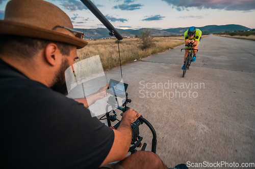 Image of A videographer recording a triathlete riding his bike preparing for an upcoming marathon.Athlete's physical endurance and the dedication required to succeed in the sport.