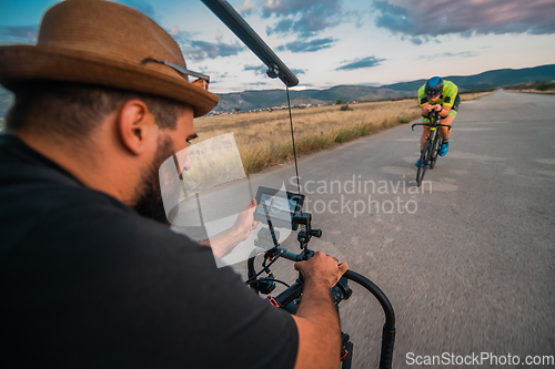 Image of A videographer recording a triathlete riding his bike preparing for an upcoming marathon.Athlete's physical endurance and the dedication required to succeed in the sport.